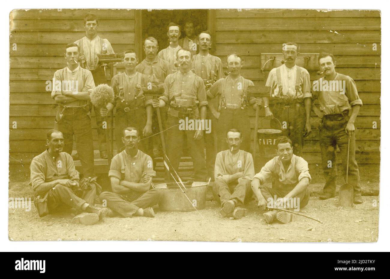 Carte postale originale de WW1 ans des soldats sur les tâches de nettoyage à l'extérieur d'une cabane, brosses, balai, pelle, bain en étain, seau de feu, l'homme a la cantine de l'armée sur la ceinture. Peut-être l'équipage de feu. À leur caserne de l'armée .UK Banque D'Images
