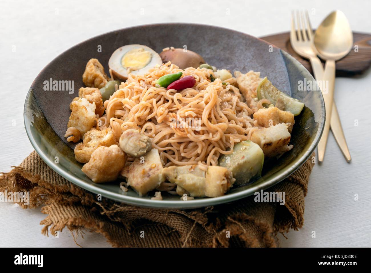 Mélanger les nouilles instantanées frites au curry vert avec du poulet (Kaeng khiao wan) et l'œuf dur à la sauce brune sucrée dans un bol en céramique servi avec un ensemble de couverts Banque D'Images