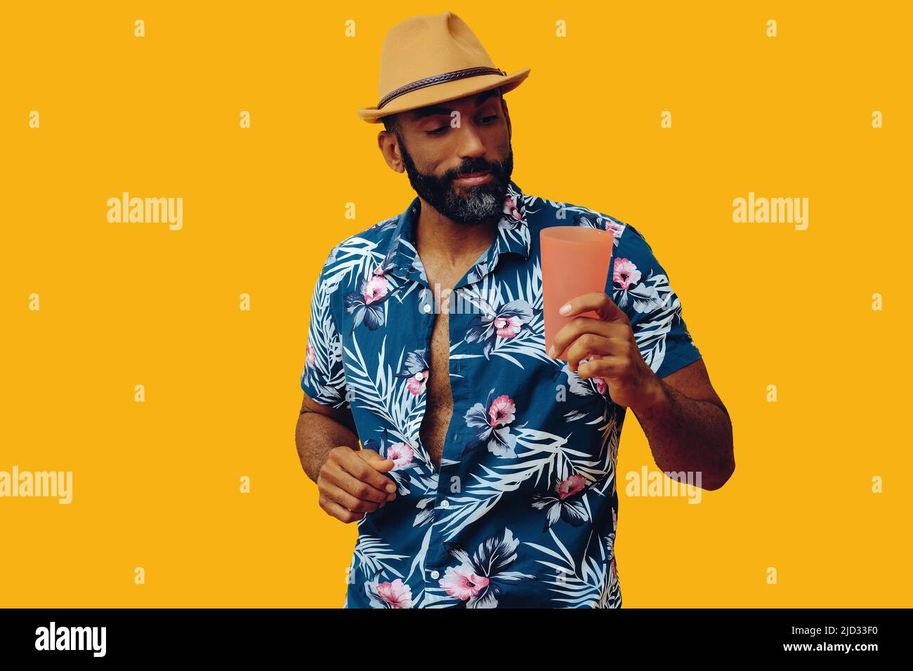 Joyeux homme afro-américain de taille moyenne adulte portant une chemise hawaïenne avec un verre à cocktail et un chapeau en studio Banque D'Images
