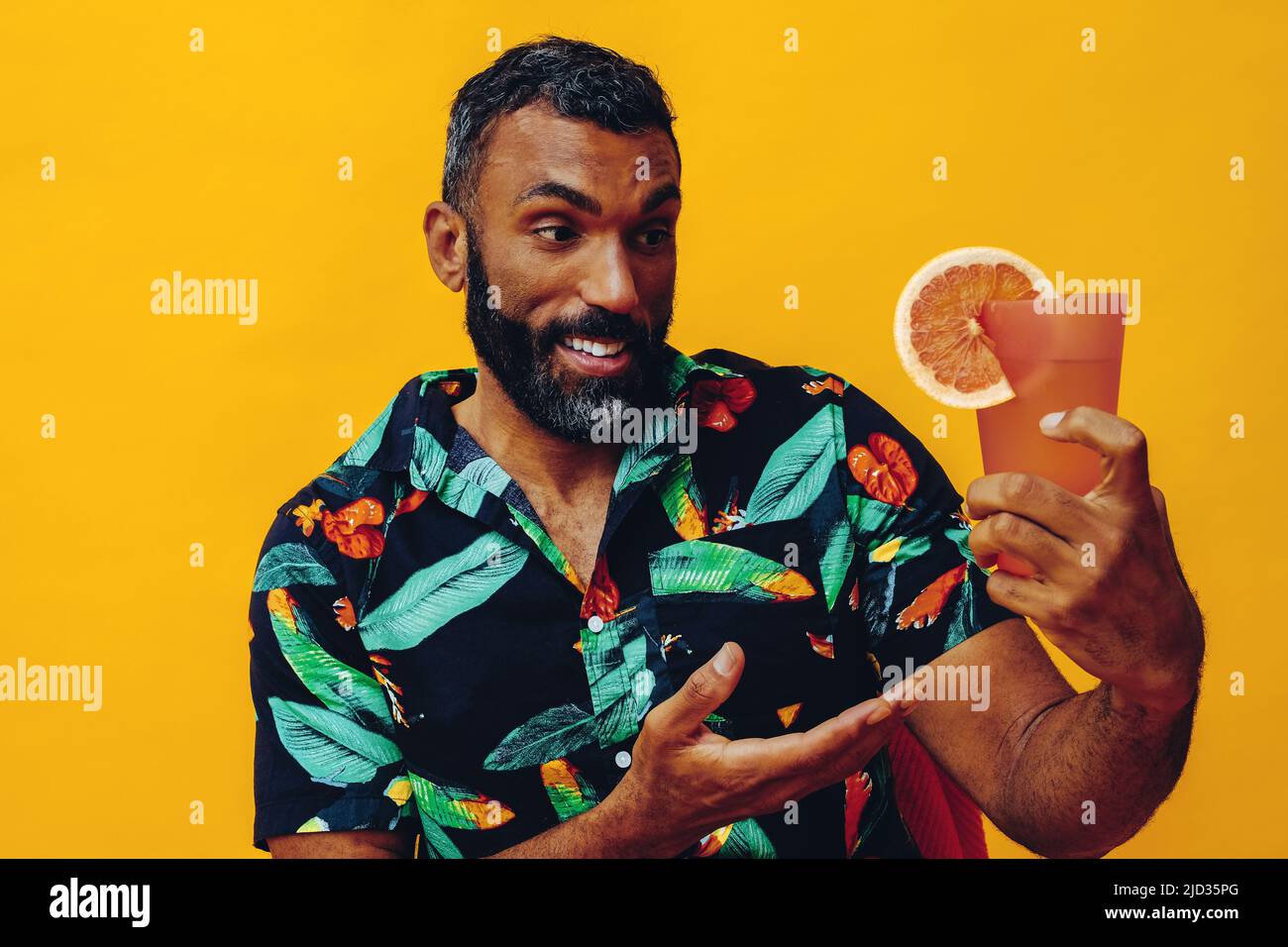 gros plan beau barbu adulte moyen afro-américain souriant pendant les vacances assis sur une chaise boire jus d'orange cocktail studio prise Banque D'Images