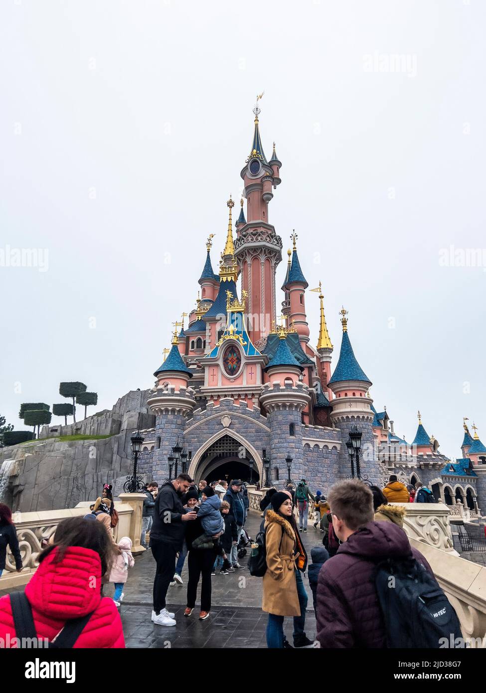 Paris, France - 04/05/2022: Personnes marchant vers le célèbre et emblématique bâtiment des parcs Disneyland. Château de la Belle au Bois dormant par temps nuageux. Banque D'Images