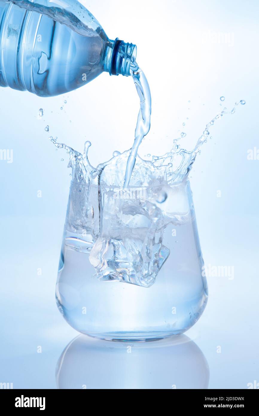 Verser l'eau minérale et les éclaboussures de la bouteille dans le verre sur fond bleu. Format vertical. Banque D'Images