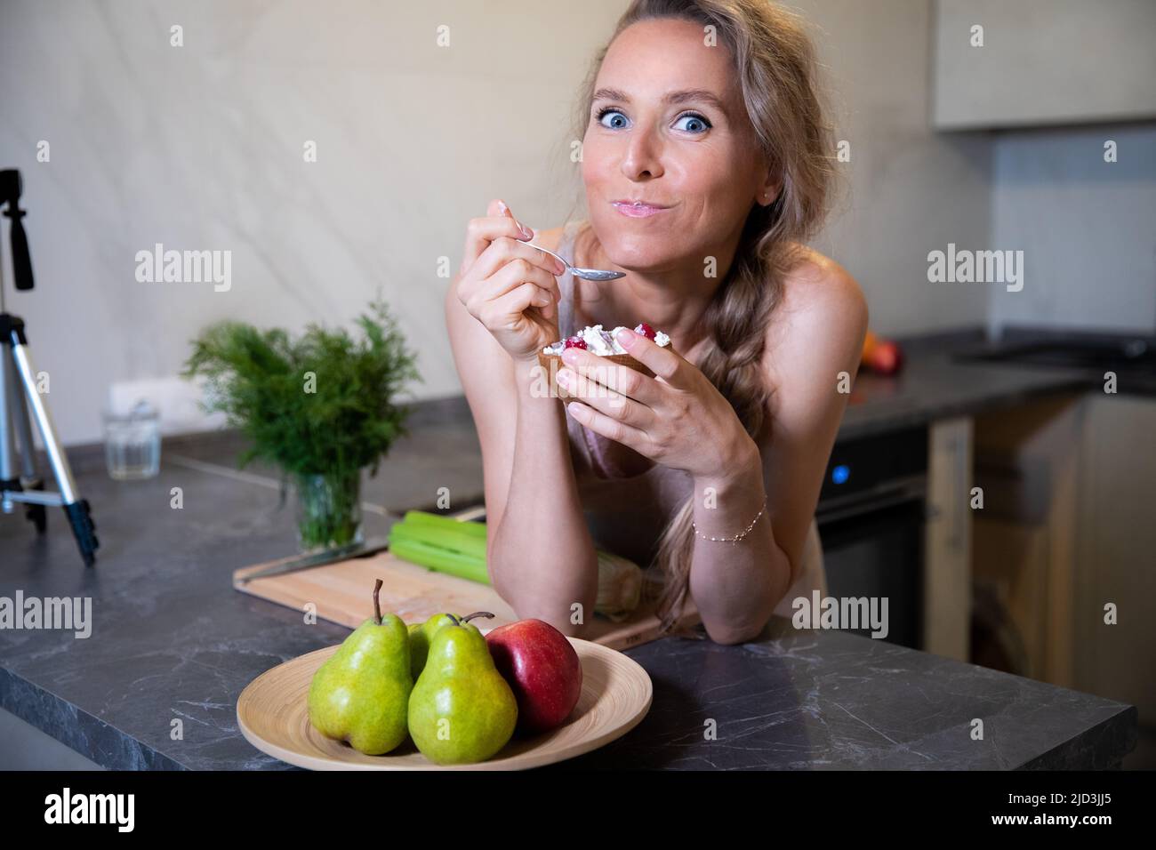 Une jeune belle blonde avec des yeux bleus d'apparence caucasienne mange avec un grand appétit frais nourriture saine à la table de cuisine à la maison. Sur la face Banque D'Images