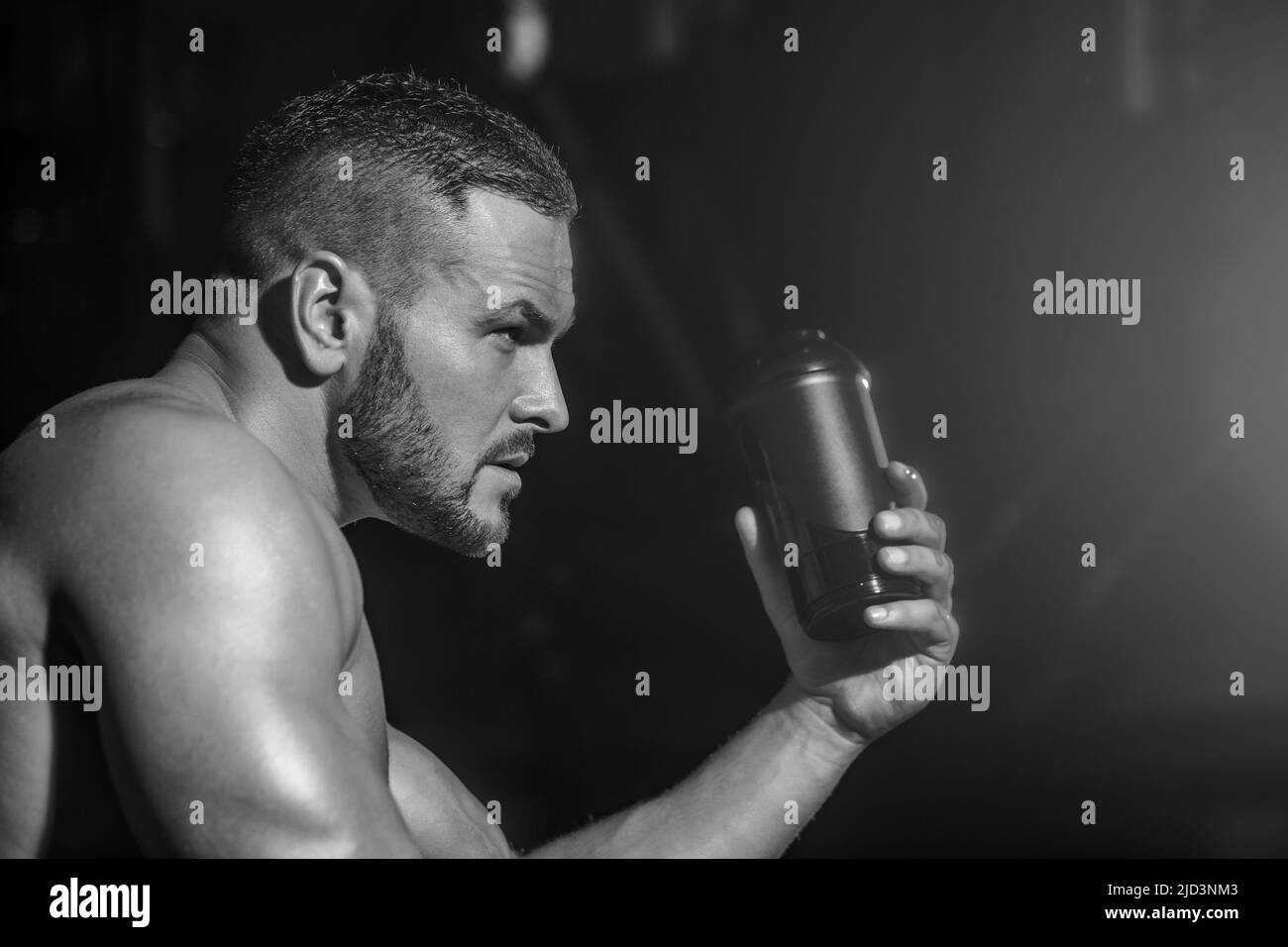 Portrait de style de vie de l'homme musclé de l'eau potable dans la salle de gym. Homme musclé boire de l'eau. Contenant de l'eau de bouteille. Noir et blanc Banque D'Images