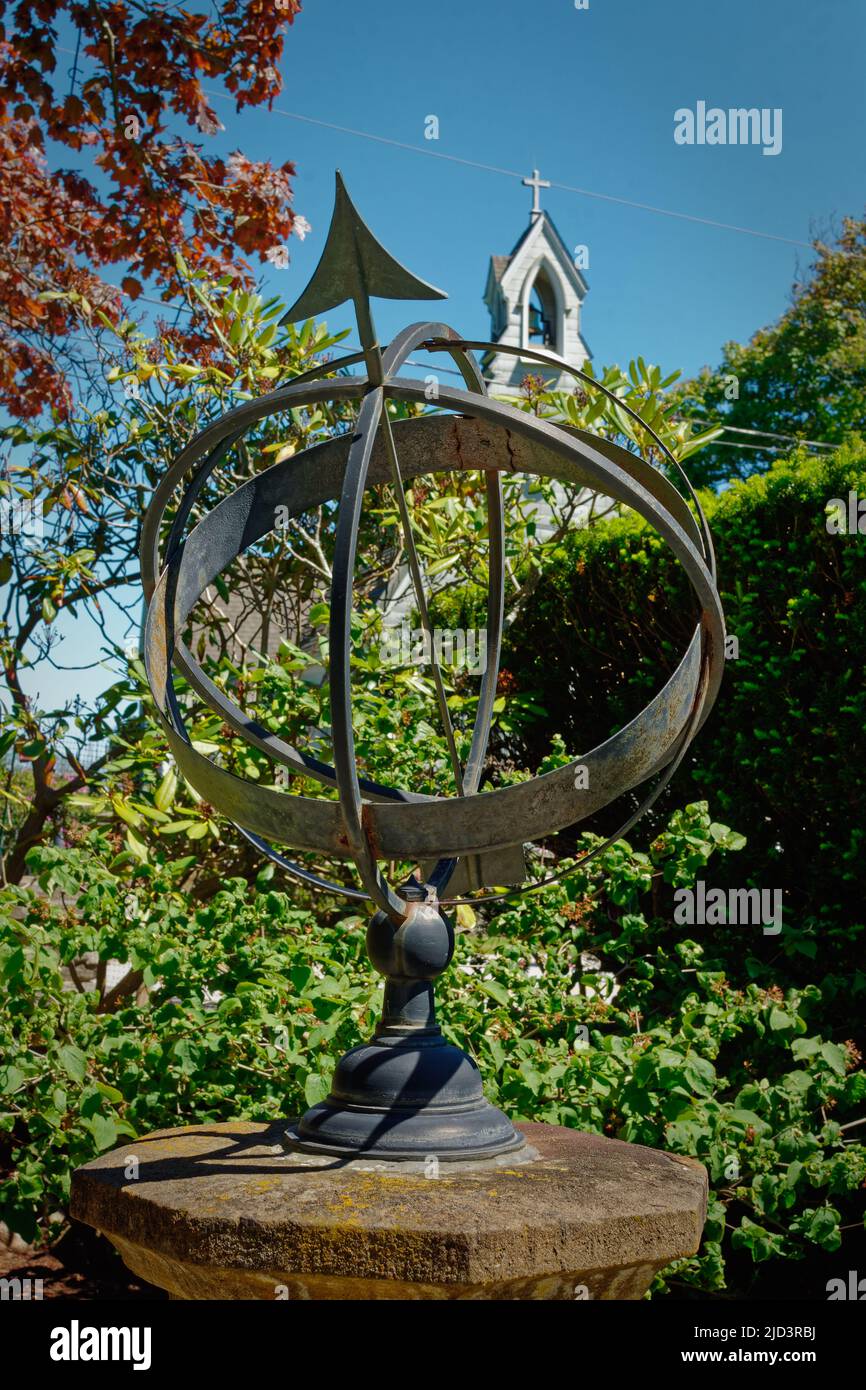 Globe métallique avec flèche pointant vers le ciel sur un piédestal dans un jardin avec une église clocher et croix dans l'arrière-plan à la propriété Fuller. N Banque D'Images