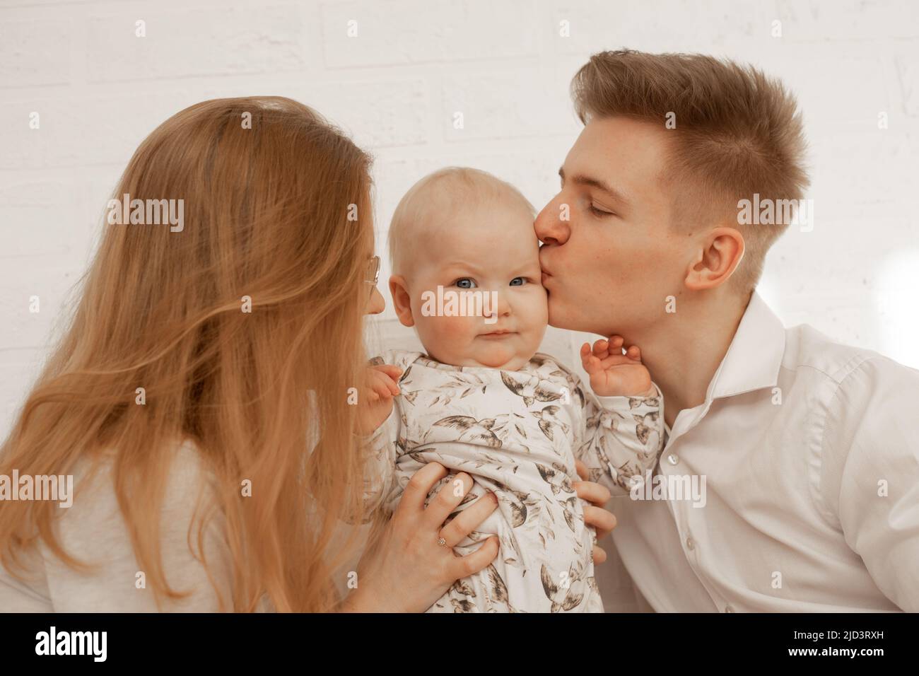 La jeune mère et le père embrassent et embrassent le petit bébé, profiter sur fond blanc. Relation mignon entre parents et enfant en bas âge, copie gratuite Banque D'Images