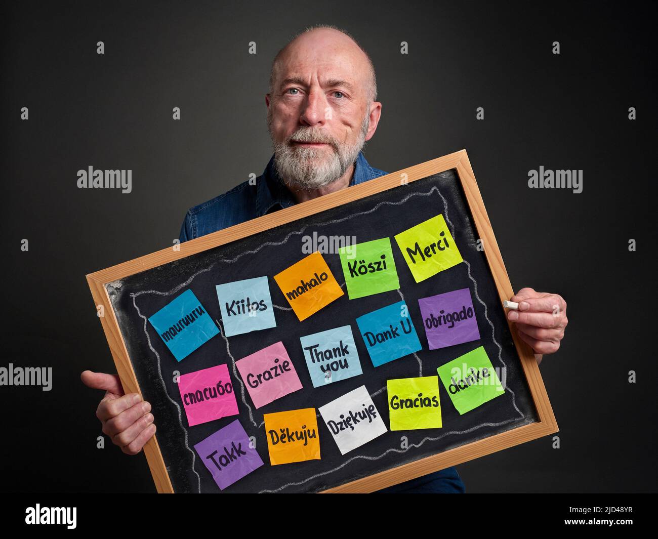 Merci en seize langues - des notes adhésives colorées sur le tableau noir tenu par un homme âgé Banque D'Images