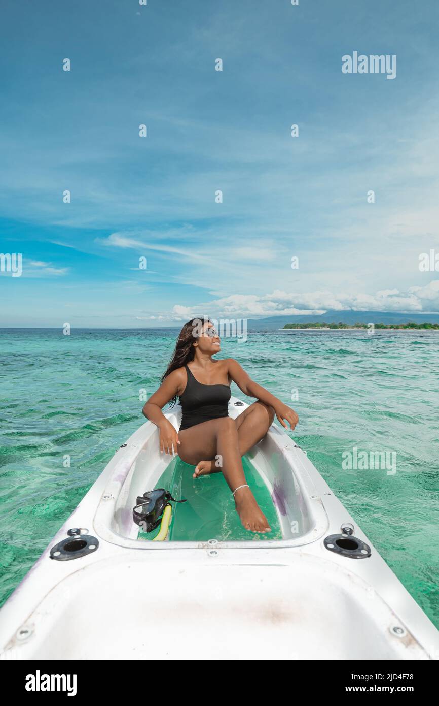 Jeune femme indonésienne en maillot de bain noir assise dans un kayak blanc avec de l'eau turquoise Banque D'Images
