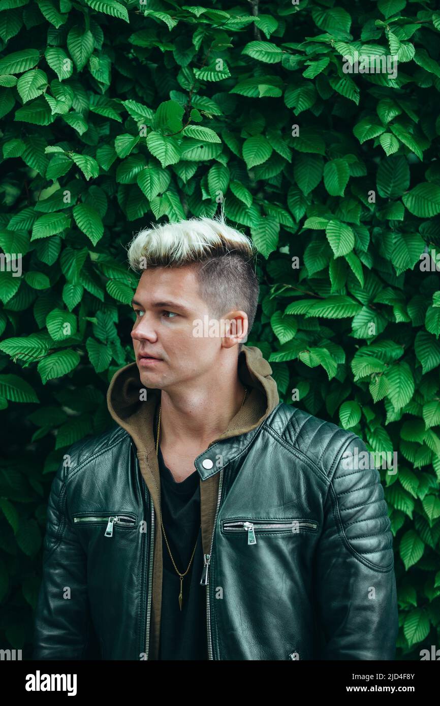 jeune homme aux cheveux blonds platine et veste en cuir noir, fond vert lierre Banque D'Images