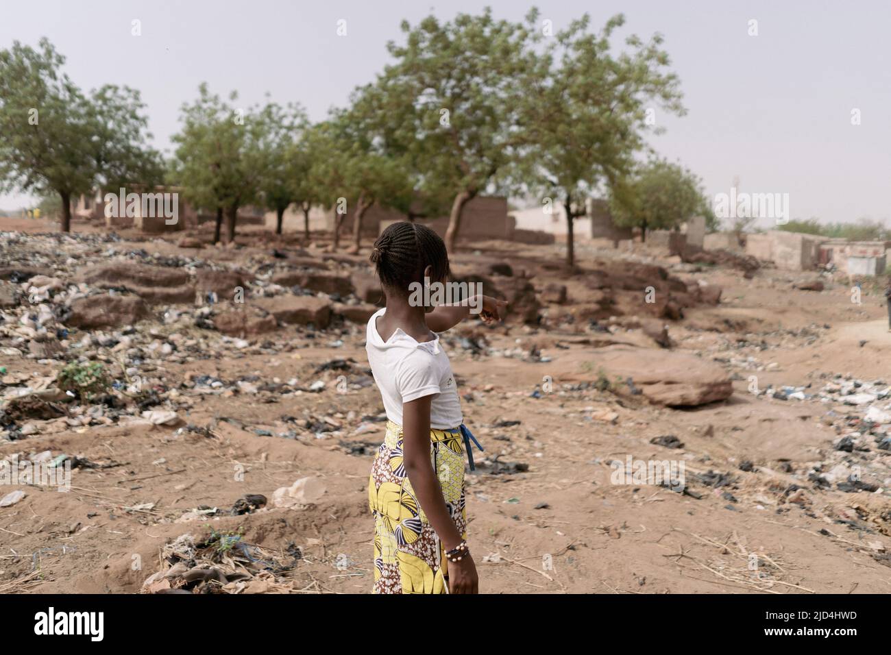 Jeune fille africaine debout avec elle dos à la caméra pointant vers le paysage déserte de sa patrie caractérisée par le changement climatique, désertique Banque D'Images