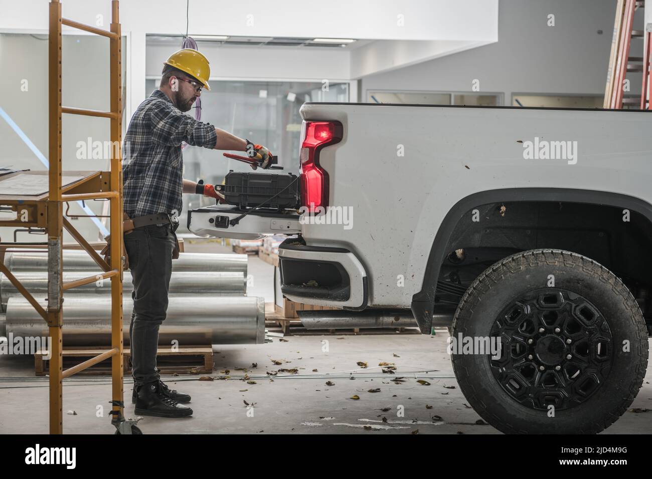 Le constructeur caucasien emballer son équipement de travail sur la caisse de son camion blanc de ramassage sur le site de construction. Banque D'Images