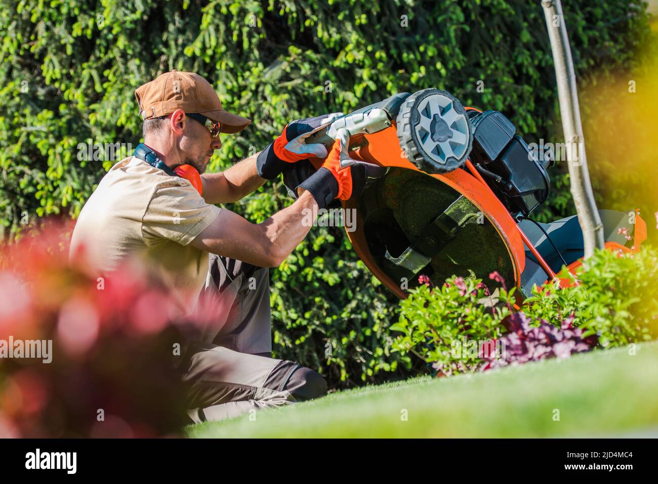 Travailleur de jardin caucasien portant des lunettes spéciales de jardinage et de sécurité vérifier l'état de son équipement de coupe d'herbe avant de commencer à tondre le Banque D'Images