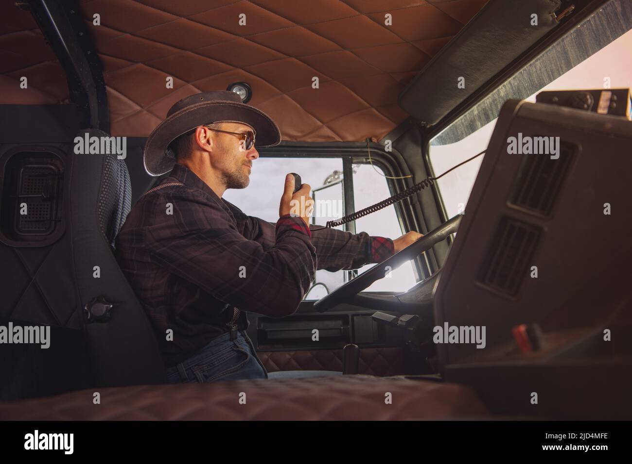 Caucasien Trucker portant un ensemble de style occidental conduite de son semi-camion et parlant par radio CB. Vue latérale. Banque D'Images