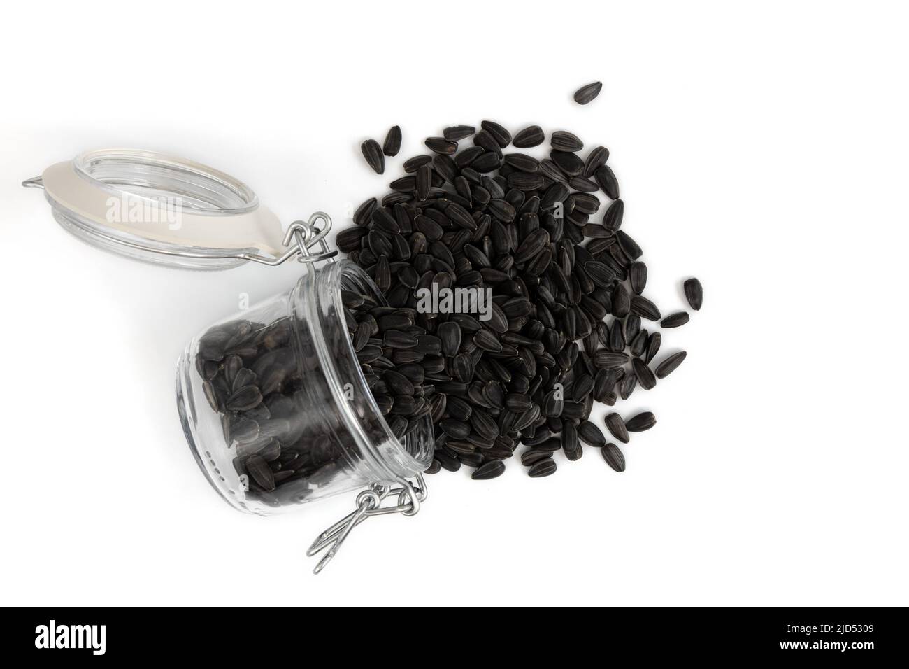graines de tournesol noires dans un pot en verre isolé sur fond blanc, vue de dessus d'une pile de graines torréfiées non pelées Banque D'Images