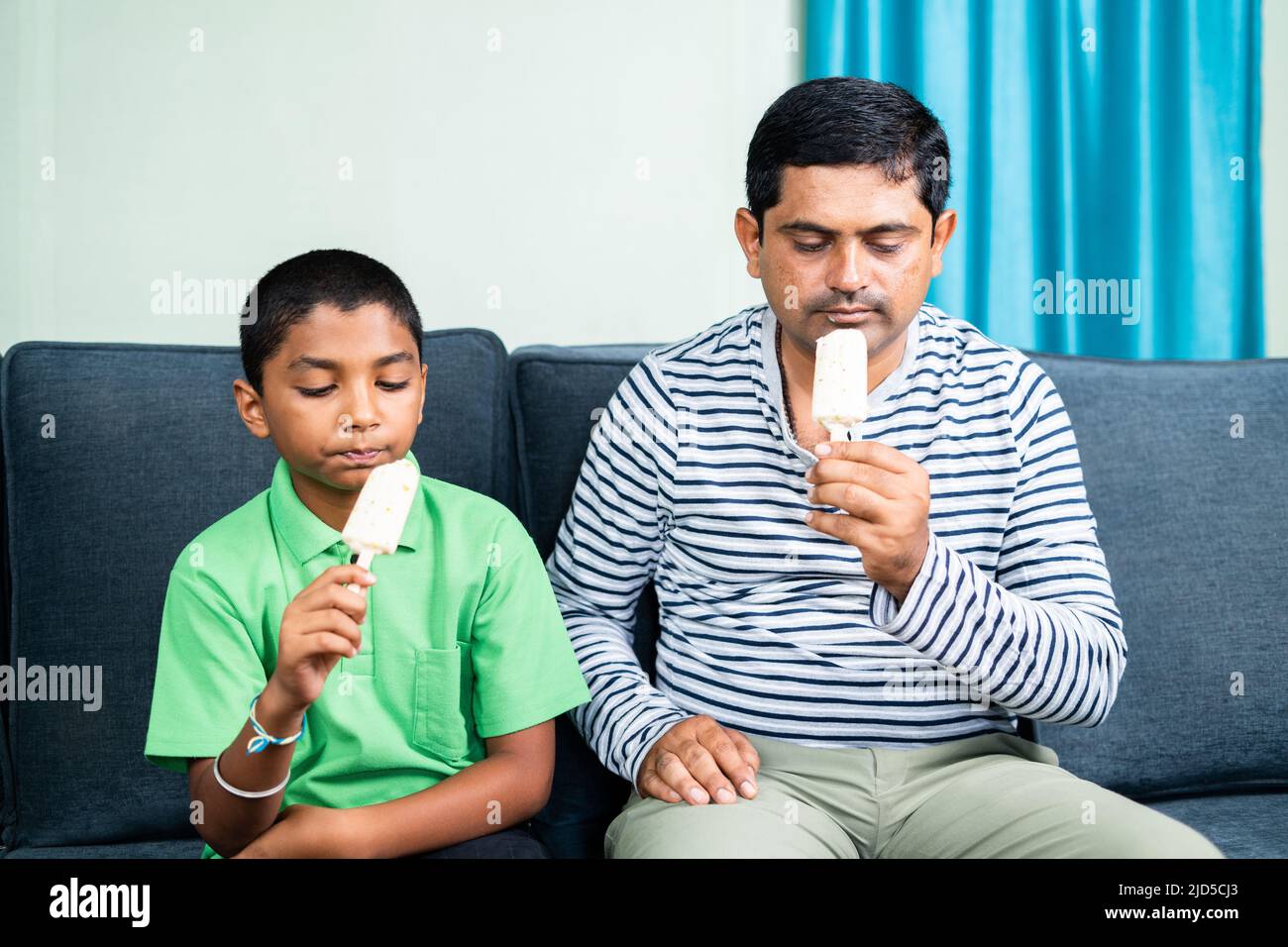 Le père et le fils s'affairent à manger des glaces à la maison tout en étant assis sur un canapé - concept d'été, de famille et de togethness. Banque D'Images