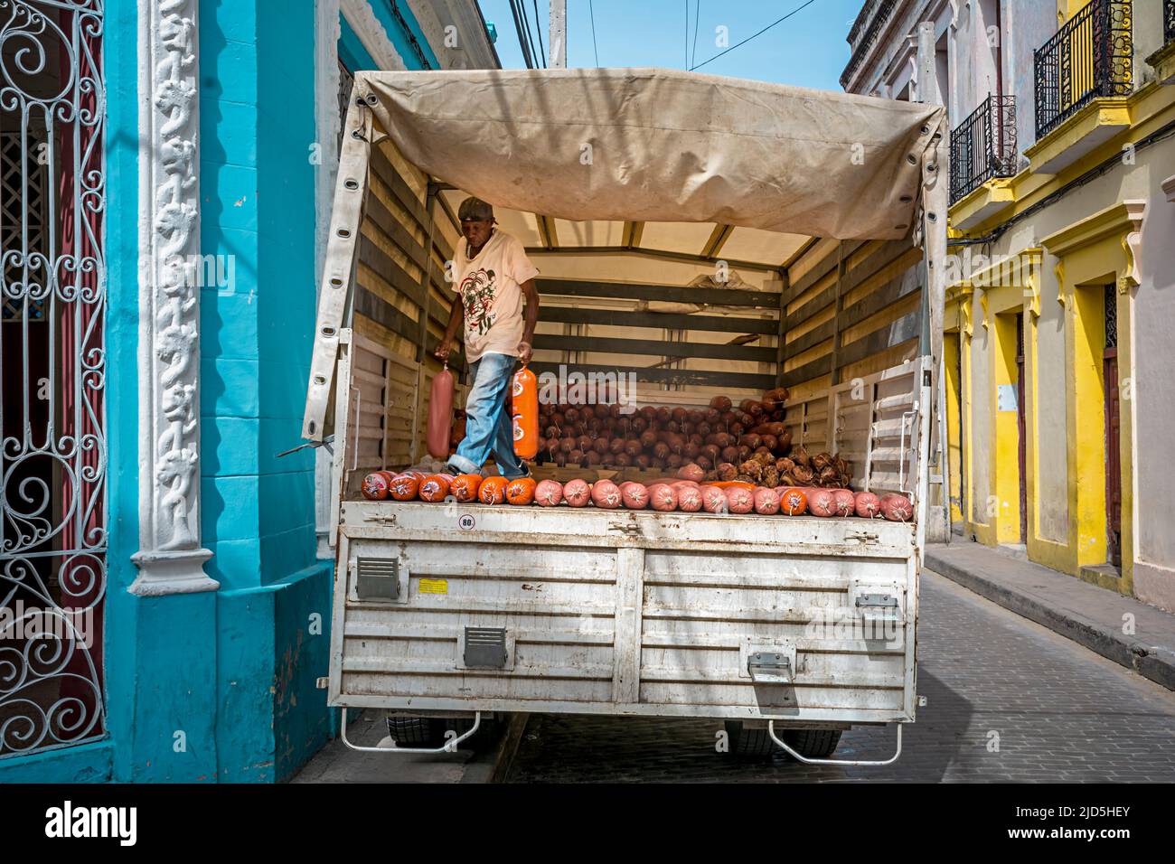 Un homme charge un camion avec de grandes saucisses dans une rue colorée à Camagüey, Cuba Banque D'Images
