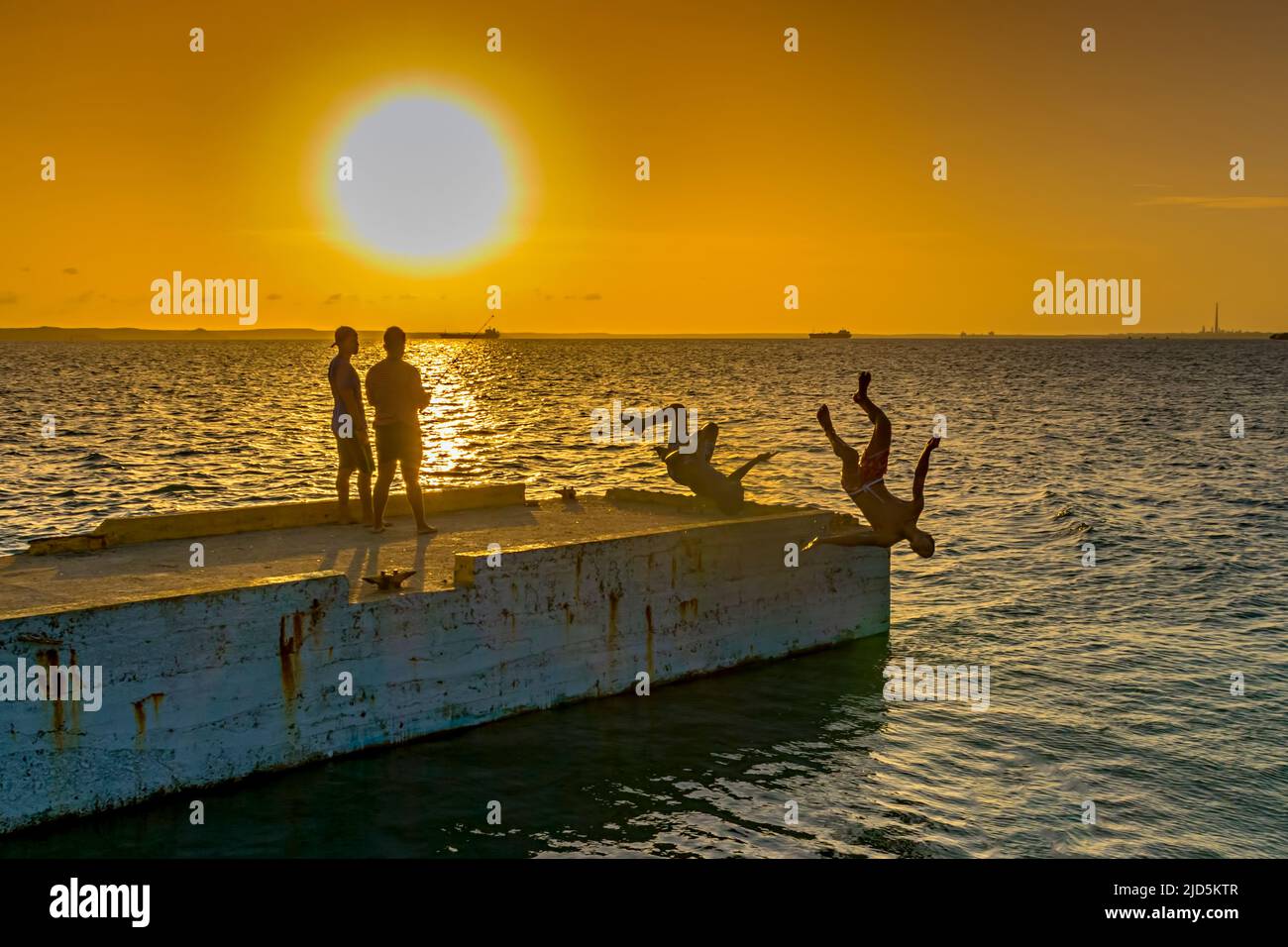 Jeunes hommes sautant sur un quai dans la mer à Cienfuegos, Cuba au coucher du soleil Banque D'Images