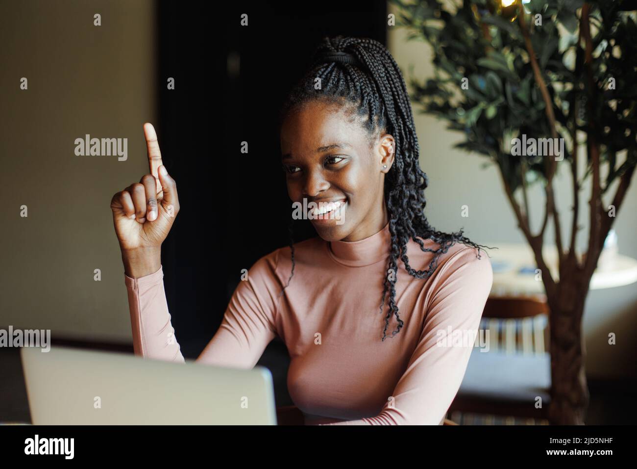 Femme afro-américaine souriante assise sur une table pointant du doigt vers le haut et travaillant dans une vue latérale du café. Fille noire travaillant à distance, freelance Banque D'Images