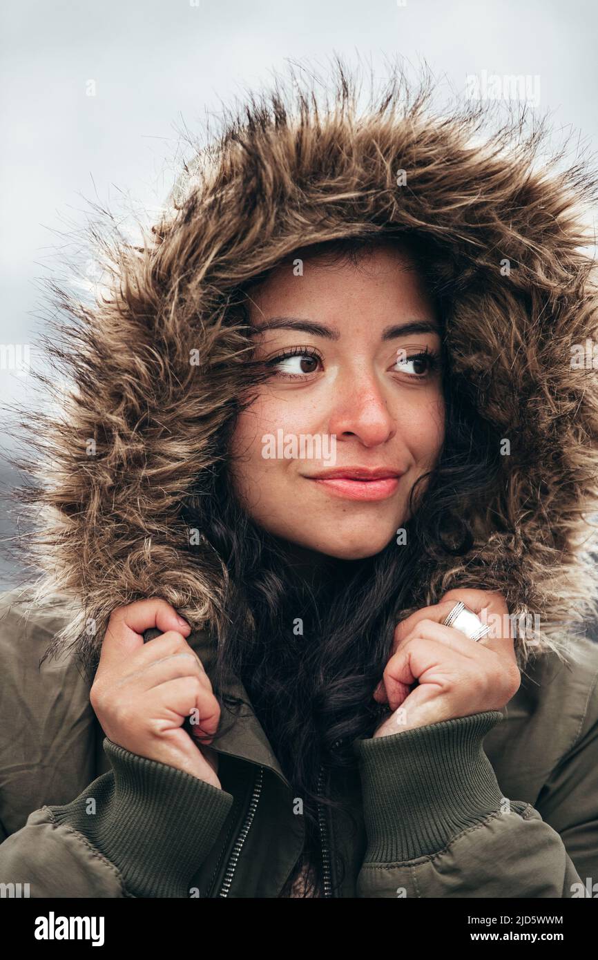 jeune femme hispanique en parka à fourrure verte en hiver froid avec fond de montagne flou Banque D'Images