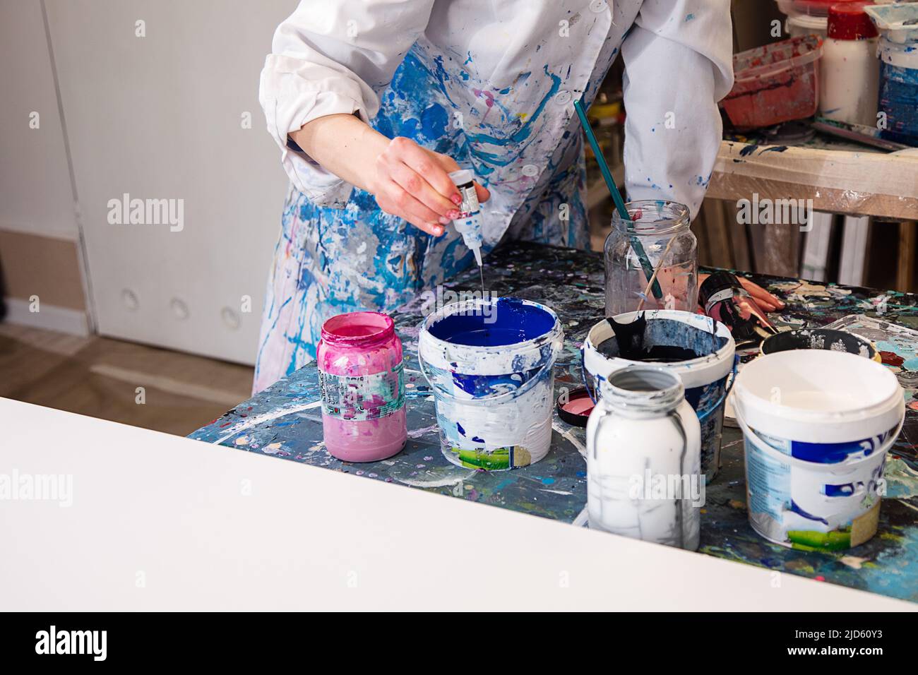 Photo rognée de femme artiste en robe blanche recouverte de diverses taches verser de plastique bouteille de peinture bleue dans le seau Banque D'Images