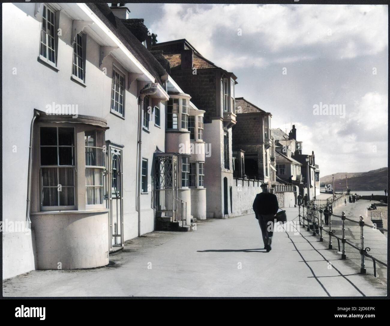 Un vieil homme avec un seau au-dessus de son bras marche le long du front de mer à Lyme Regis, Dorset, Angleterre. Version colorisée de : 10155526 Date: 1950s Banque D'Images