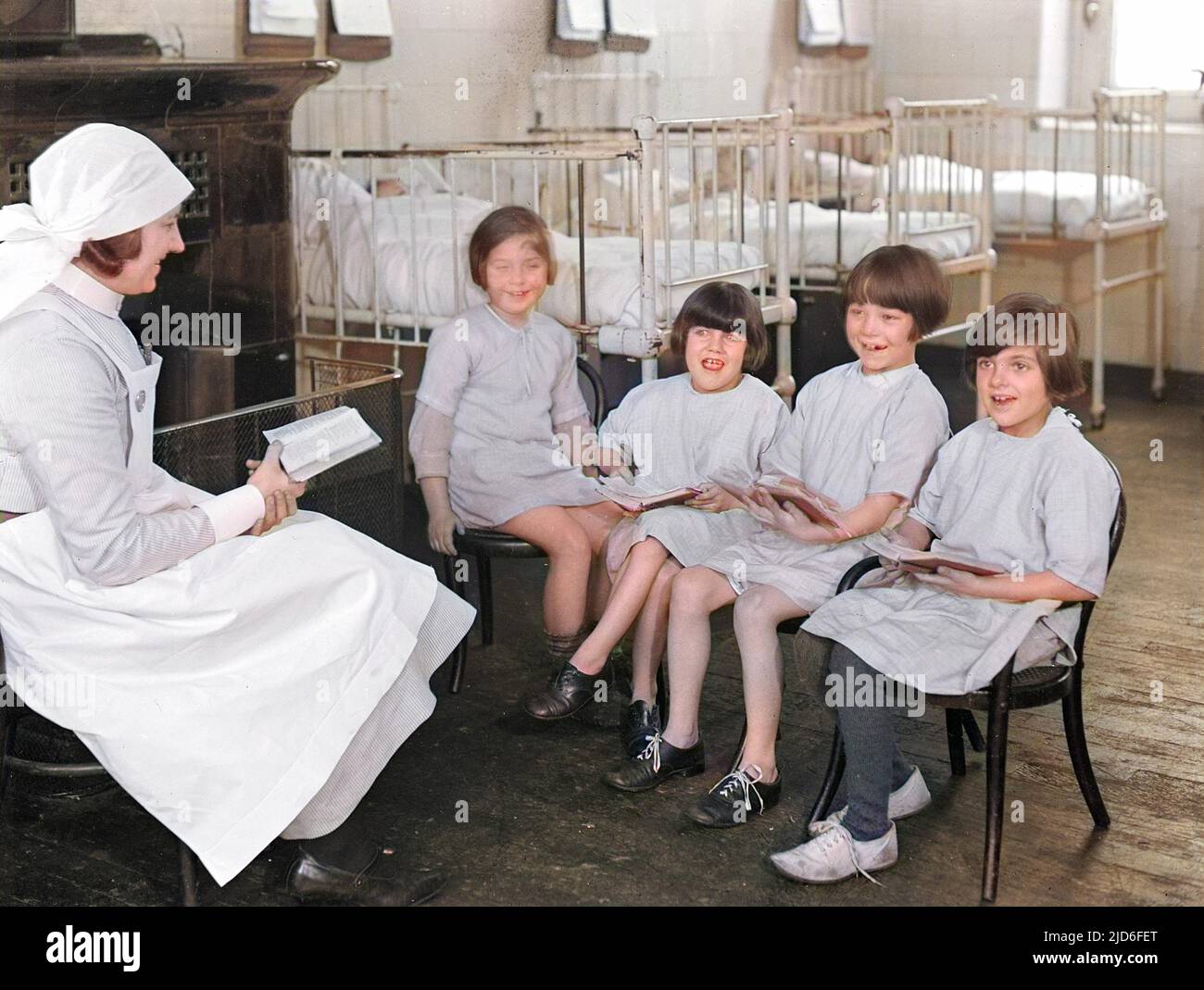 Quatre petites filles bénéficiant d'une leçon de lecture à l'hôpital, avec leur infirmière doublant en tant qu'enseignante. Version colorisée de : 10164371 Date : début 1930s Banque D'Images