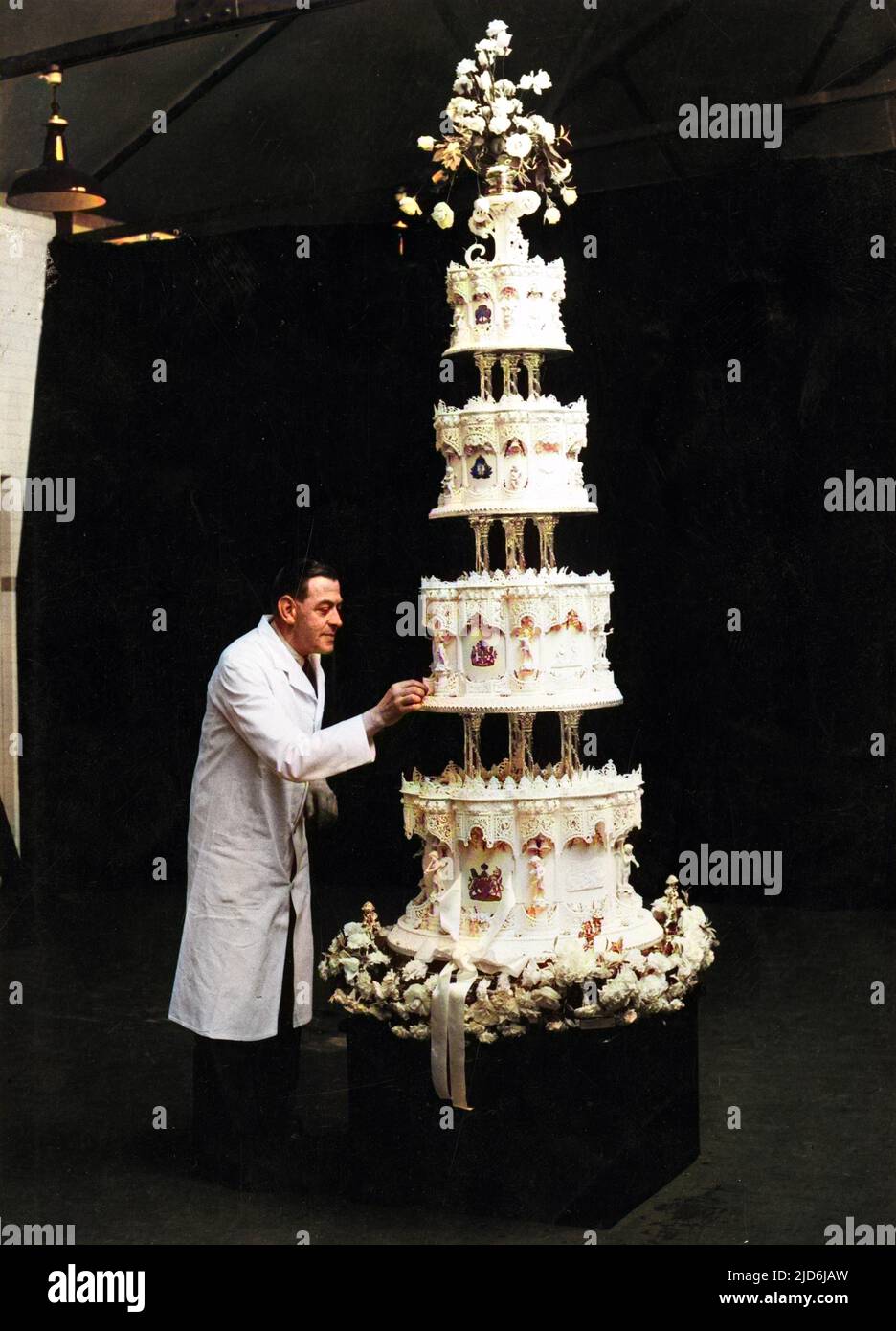 Gâteau de mariage fait par M. F. Schul de McVitie et Price à Harlesden, Londres pour le mariage de la princesse Elizabeth au lieutenant Philip Mountbatten en novembre 1947. Mesurant 9 pieds de haut et 500lb de poids, le gâteau à quatre niveaux se tenait en état pour être photographié, gardé par la police, les chaînes et M. Schul lui-même. Tous les ingrédients du gâteau, qui a pris dix heures à cuire, venaient des dominions. La décoration a pris quatre à cinq semaines. L'image montre M. Schul ajoutant les touches de finition au gâteau. Version colorisée de : 10509458 Date: 1947 Banque D'Images