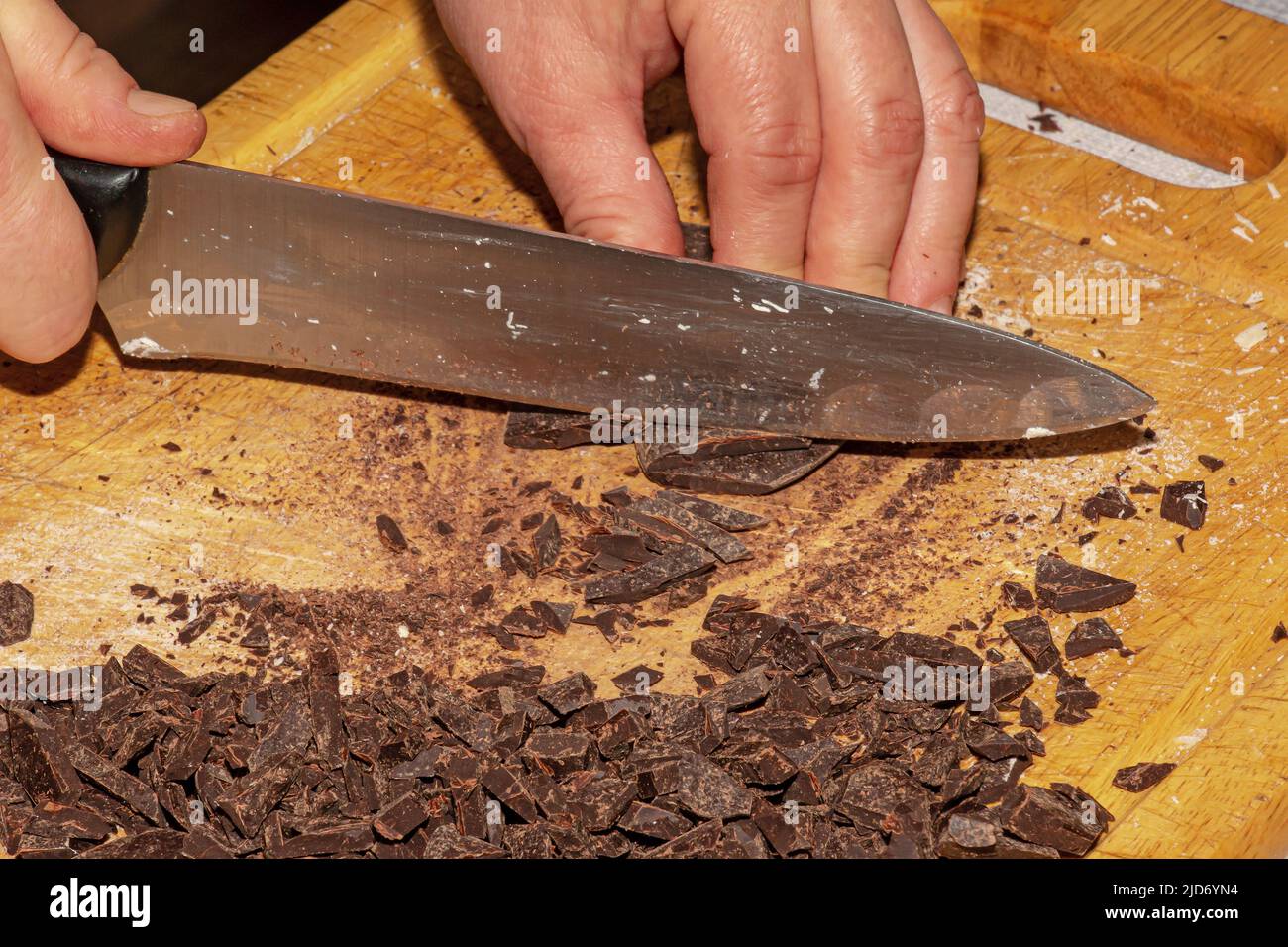 Les mains de la cuisinière écrasent le cacao râpé avec un couteau sur une planche de cuisine en bois pour faire du chocolat. Banque D'Images