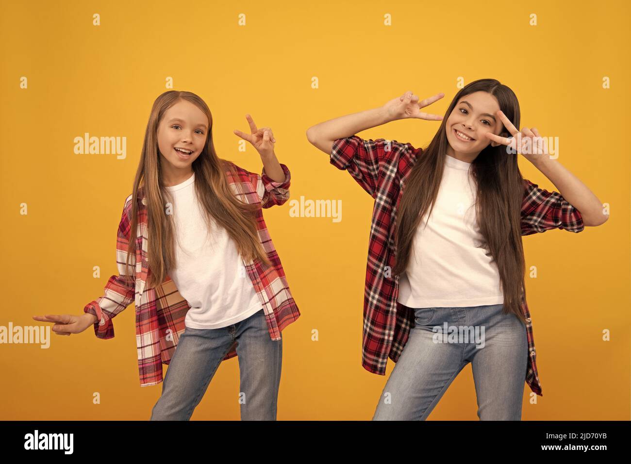 bonne adolescente filles dans une chemise décontractée ayant l'amusement montrant le geste de paix sur fond jaune, l'enfance. Banque D'Images