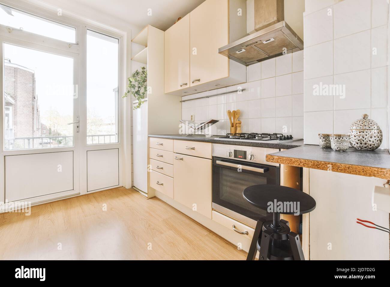 Intérieur d'une cuisine lumineuse avec parquet, armoires et portes-balcons dans un appartement moderne pendant la journée Banque D'Images