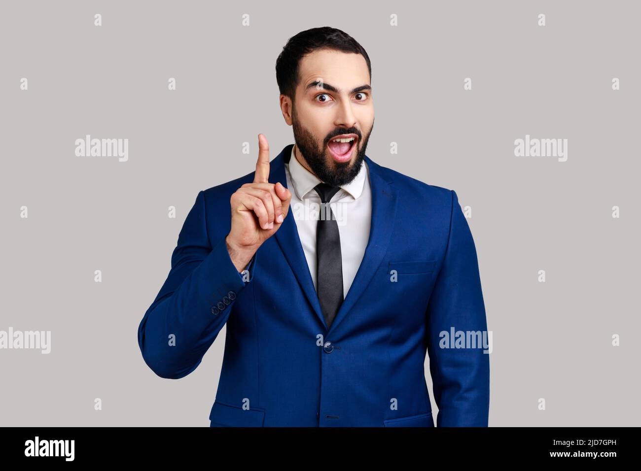 Portrait de l'homme barbu pointant du doigt vers le haut et regardant stupéfait par idée de génie soudain, a trouvé la solution, portant le costume de style officiel. Prise de vue en studio isolée sur fond gris. Banque D'Images