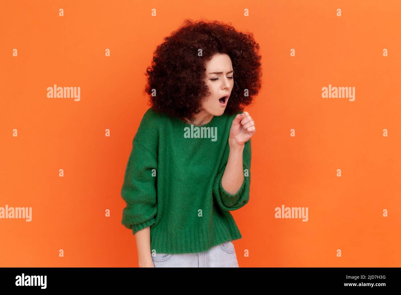Portrait d'une femme malade avec une coiffure afro portant un chandail vert de style décontracté qui attrape le froid, tousse, ayant une température élevée, a besoin d'un traitement. Studio d'intérieur isolé sur fond orange. Banque D'Images