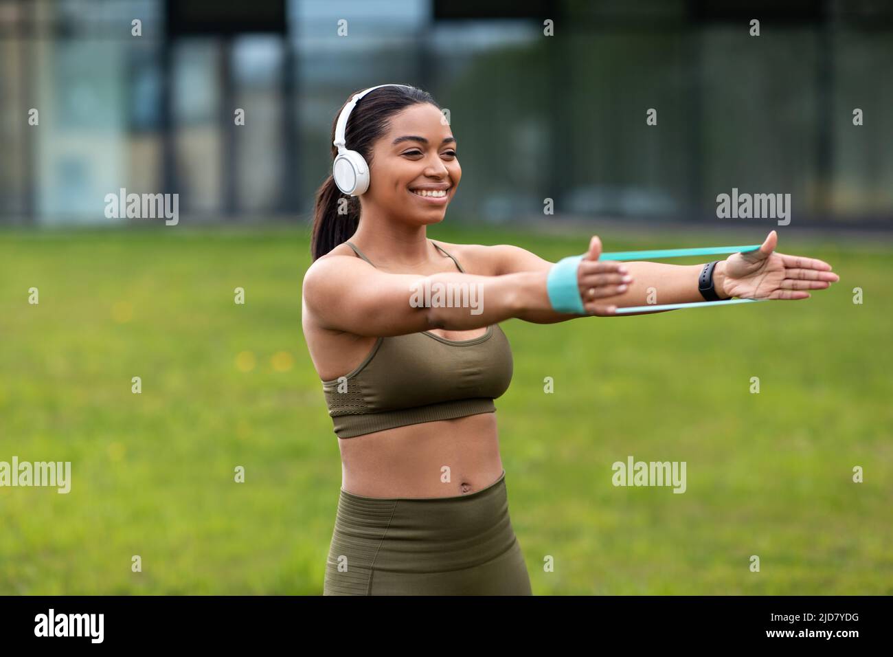 Femme noire millénaire sportive s'entraîner avec un élastique, écouter de la musique pendant l'entraînement en plein air, espace libre Banque D'Images