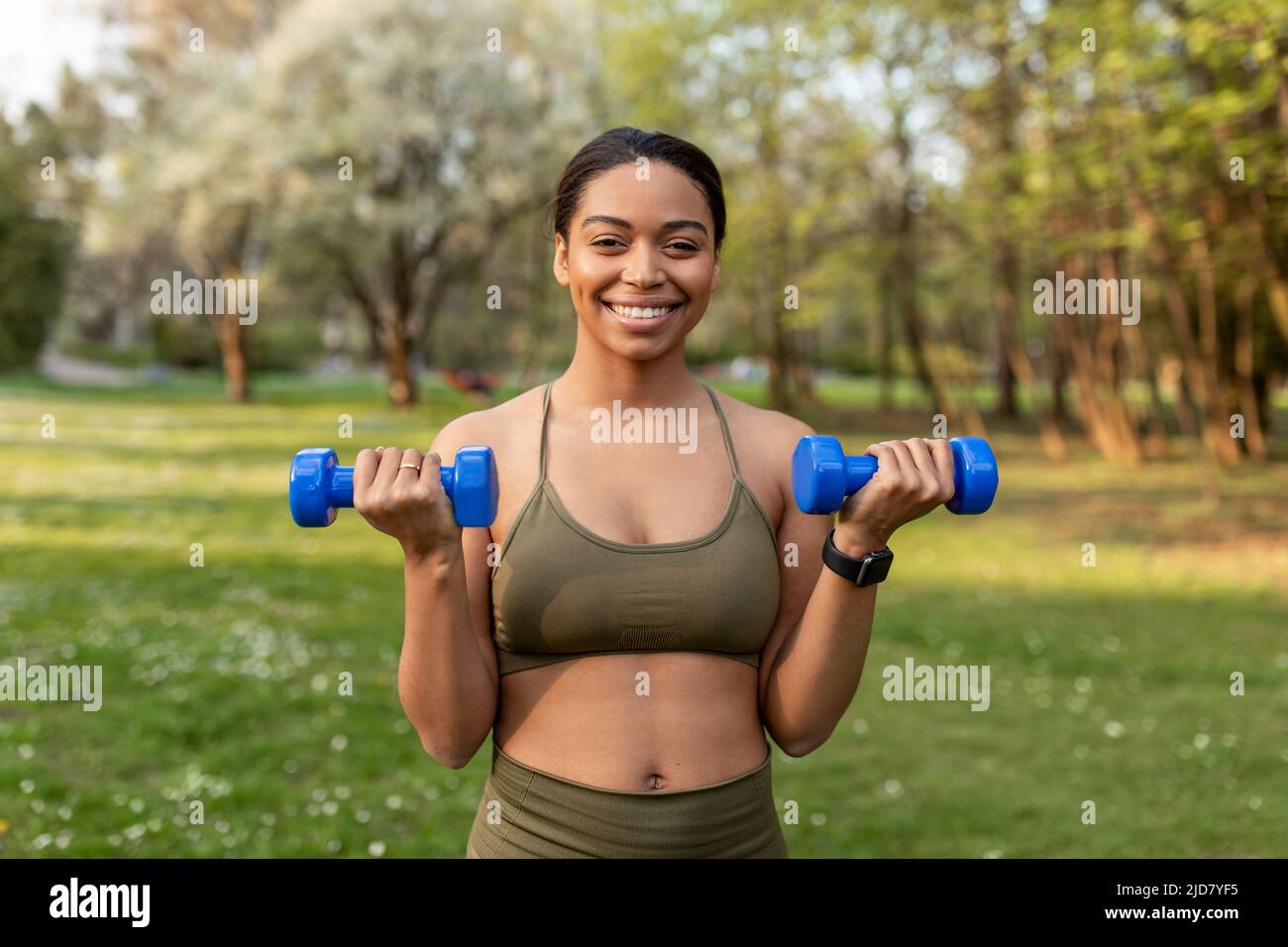 Tricherie jeune femme noire faisant de l'entraînement de force en plein air, s'exerçant avec des haltères, l'exercice de muscles au parc de la ville Banque D'Images