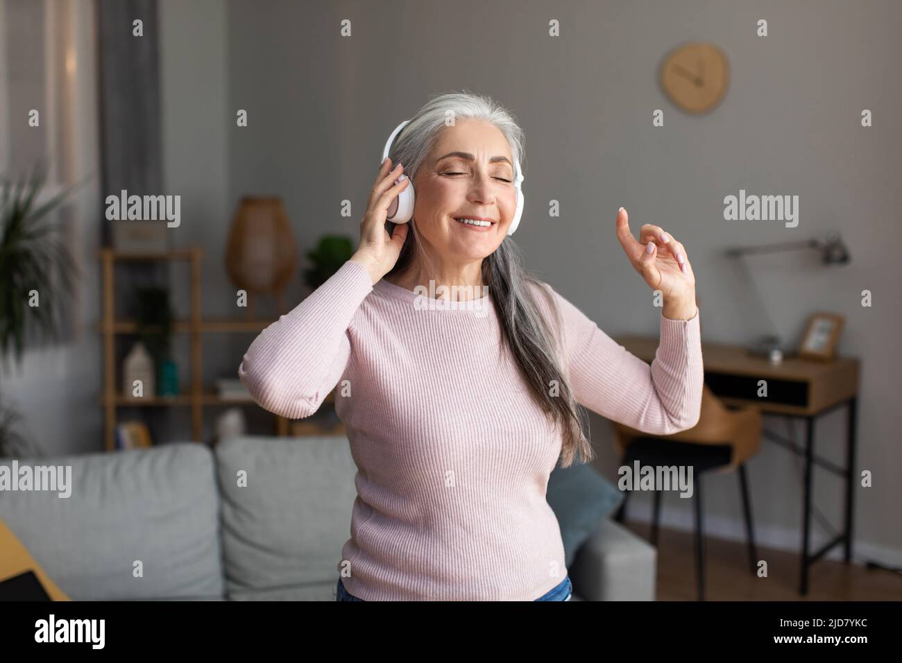 Une femme européenne aux cheveux gris et aux écouteurs sans fil est heureuse d'écouter votre musique préférée et de profiter de son temps libre Banque D'Images