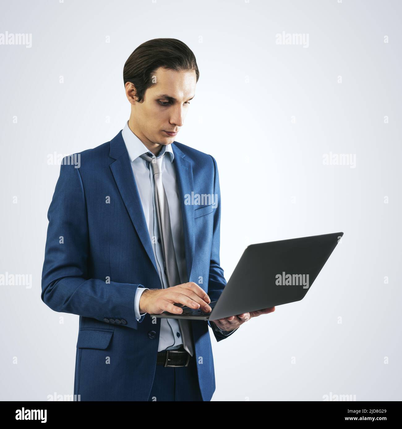 Jeune homme d'affaires en costume bleu travaillant avec un ordinateur portable moderne, isolé sur fond de mur gris clair, gros plan Banque D'Images