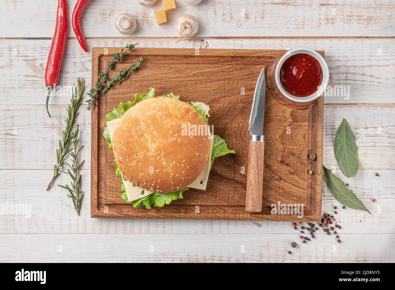 planche à découper carrée en bois de couleur foncée avec bordure. hamburger avec salade et côtelettes, champignons, piment et épices sur fond blanc, top vie Banque D'Images