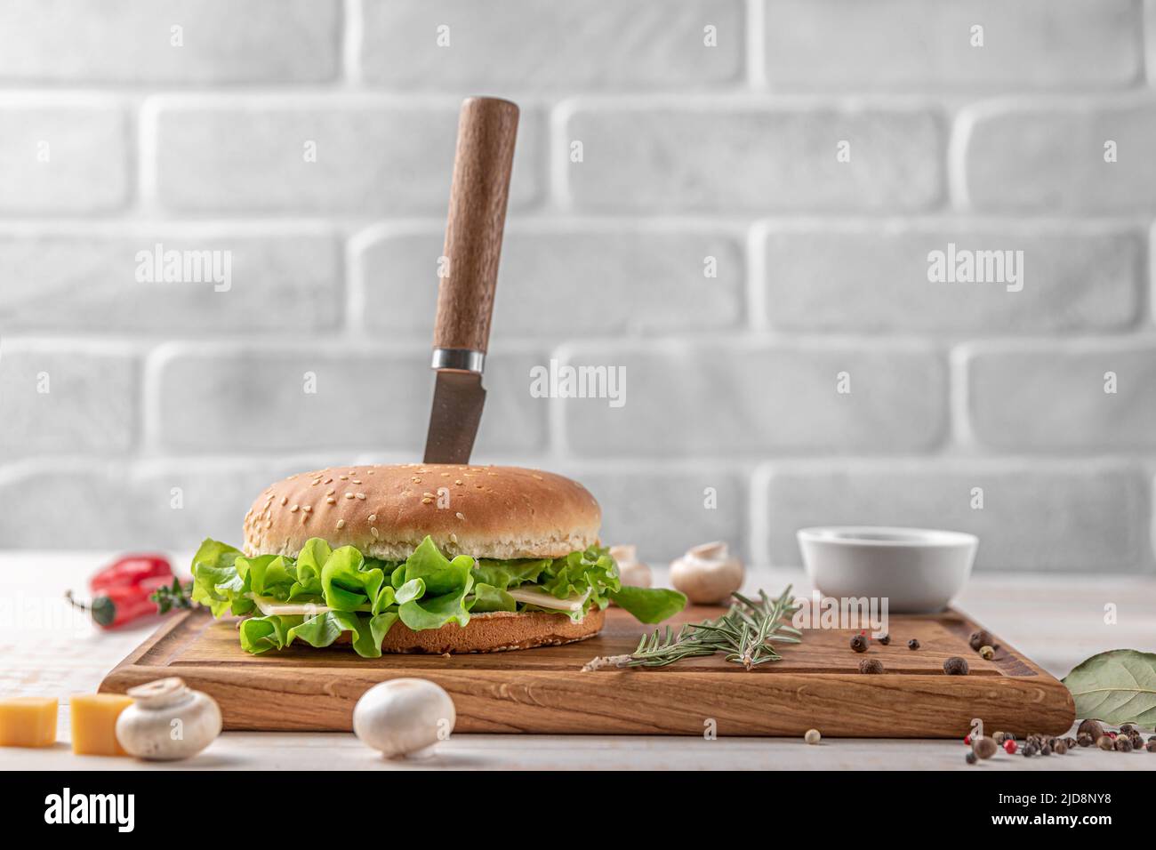 planche à découper carrée en bois de couleur foncée avec bordure. hamburger avec salade et côtelettes, champignons, piment et épices sur fond blanc, côté vi Banque D'Images