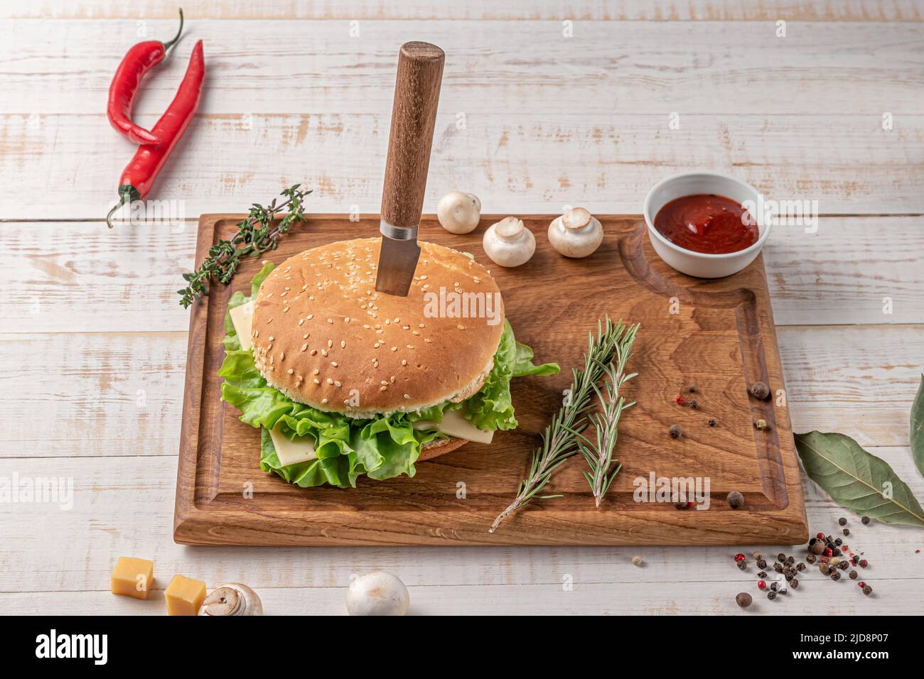 planche à découper carrée en bois de couleur foncée avec bordure. hamburger avec salade et côtelettes, champignons, piment et épices sur fond blanc, côté vi Banque D'Images
