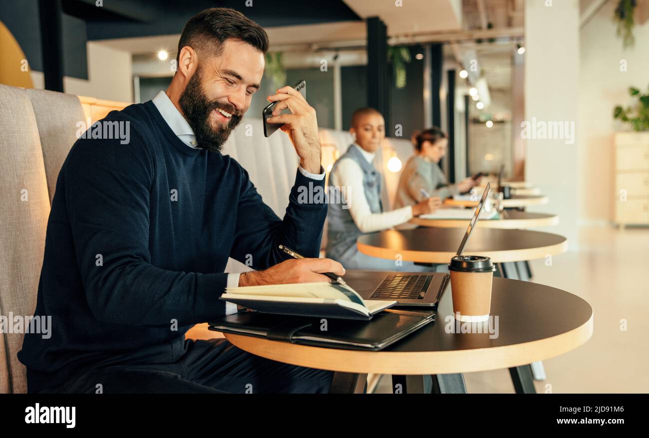 Homme d'affaires heureux de prendre des notes pendant un appel téléphonique. Jeune homme d'affaires souriant gaiement tout en faisant des plans avec ses associés au téléphone. Jeune Banque D'Images