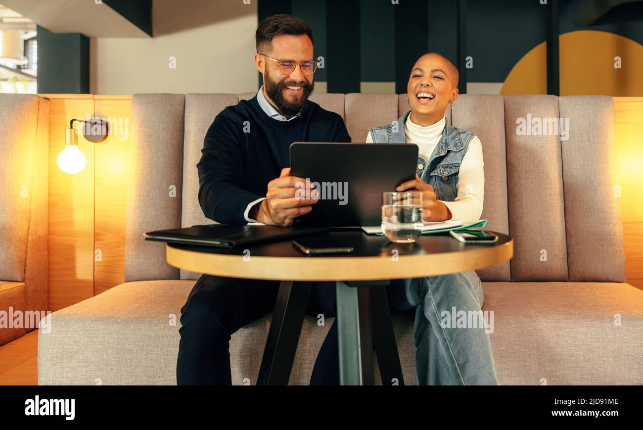 Les entrepreneurs qui prennent un appel vidéo sur une tablette numérique. Deux jeunes créatifs sourient volontiers lors d'une conférence en ligne avec leurs associés. Joyeux Banque D'Images