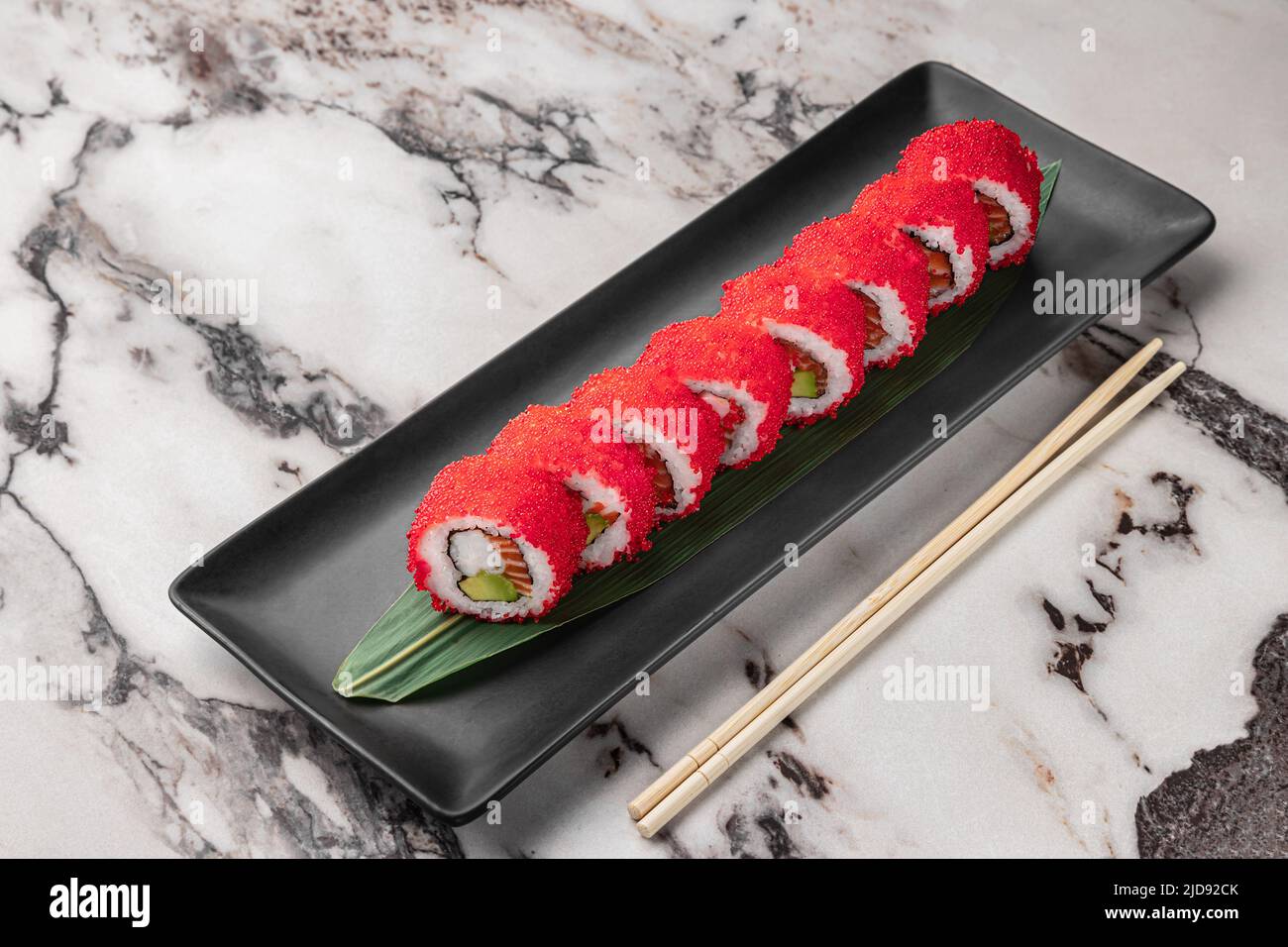 ensemble de rouleaux de philadelphie avec caviar de poisson volant rouge, avocat, saumon et feuille de bambou vert dans une plaque en céramique noire avec baguette sur un textu brillant Banque D'Images