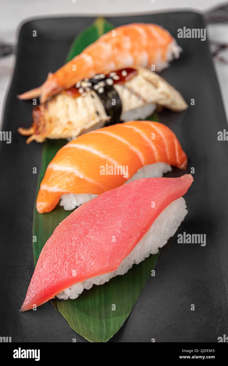 ensemble de nigiri avec crevettes tigrées, tomago, saumon, thon et feuille de bambou verte dans une assiette en céramique noire avec baguette sur un marbre blanc brillant texturé Banque D'Images