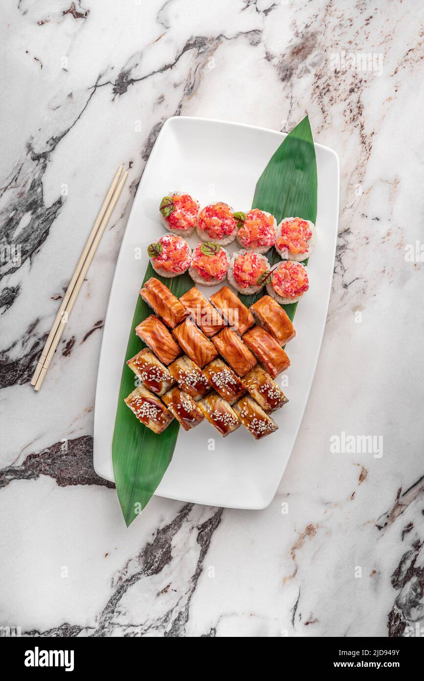 ensemble de différents petits pains à sushis maki colorés avec thon, saumon, crevettes, crabe et avocat et feuilles de bambou vertes dans une assiette en céramique blanche avec bâton de chopo Banque D'Images