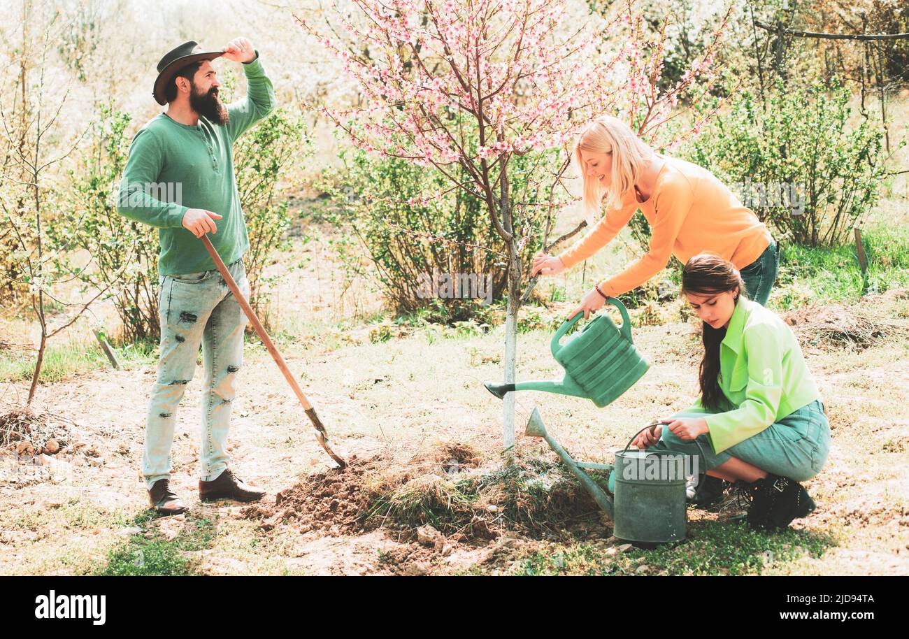 Plantez un arbre. Un groupe d'amis apprécient la nature printanière et prennent soin des plantes. Une fille qui arrose des plantes dans le jardin au printemps par beau temps. Amis Banque D'Images