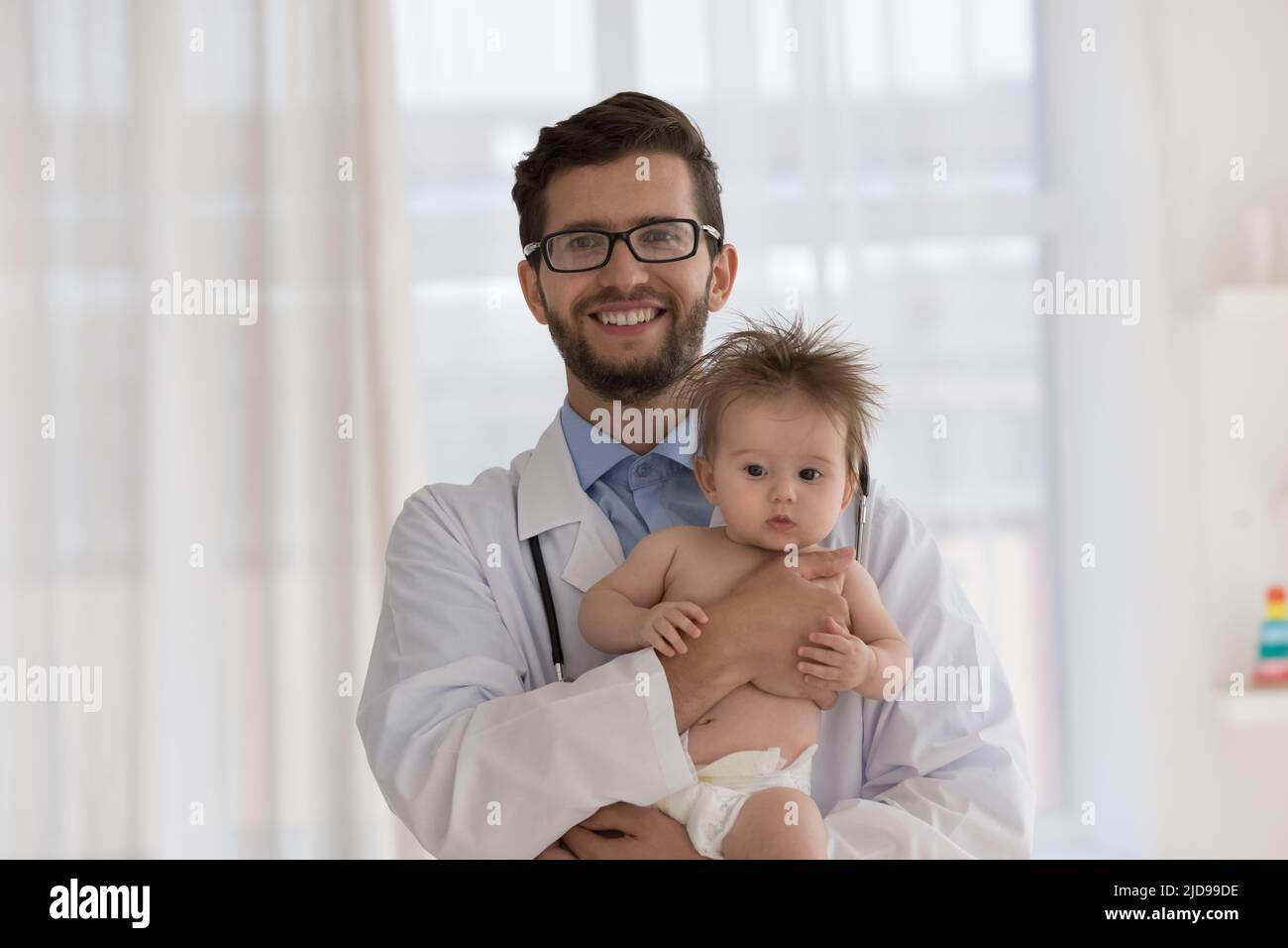 Pédiatre en uniforme blanc tenant bébé mignon regarde l'appareil photo Banque D'Images