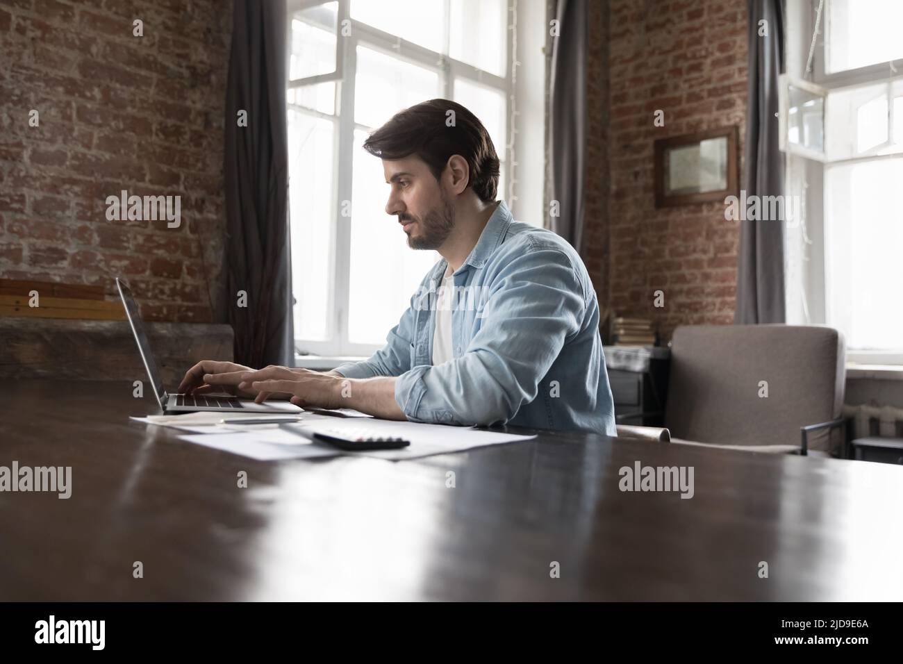 Homme d'affaires utilisant un ordinateur portable s'asseoir à un bureau avec des papiers et une calculatrice Banque D'Images