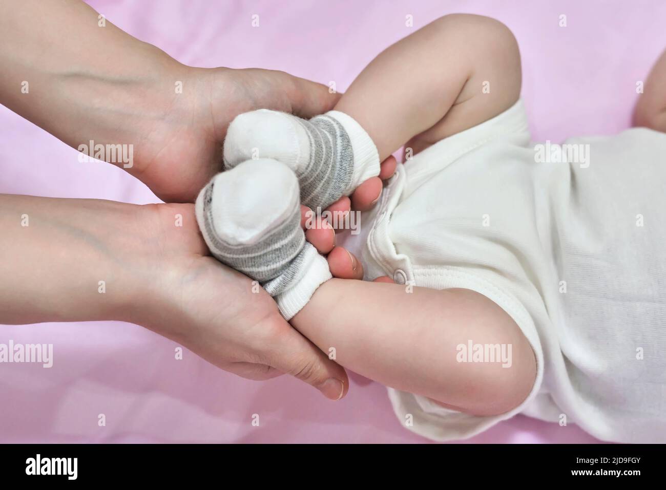 une femme met des chaussettes et une barboteuse pour bébé qui fait un massage des pieds à son petit enfant gros plan Banque D'Images