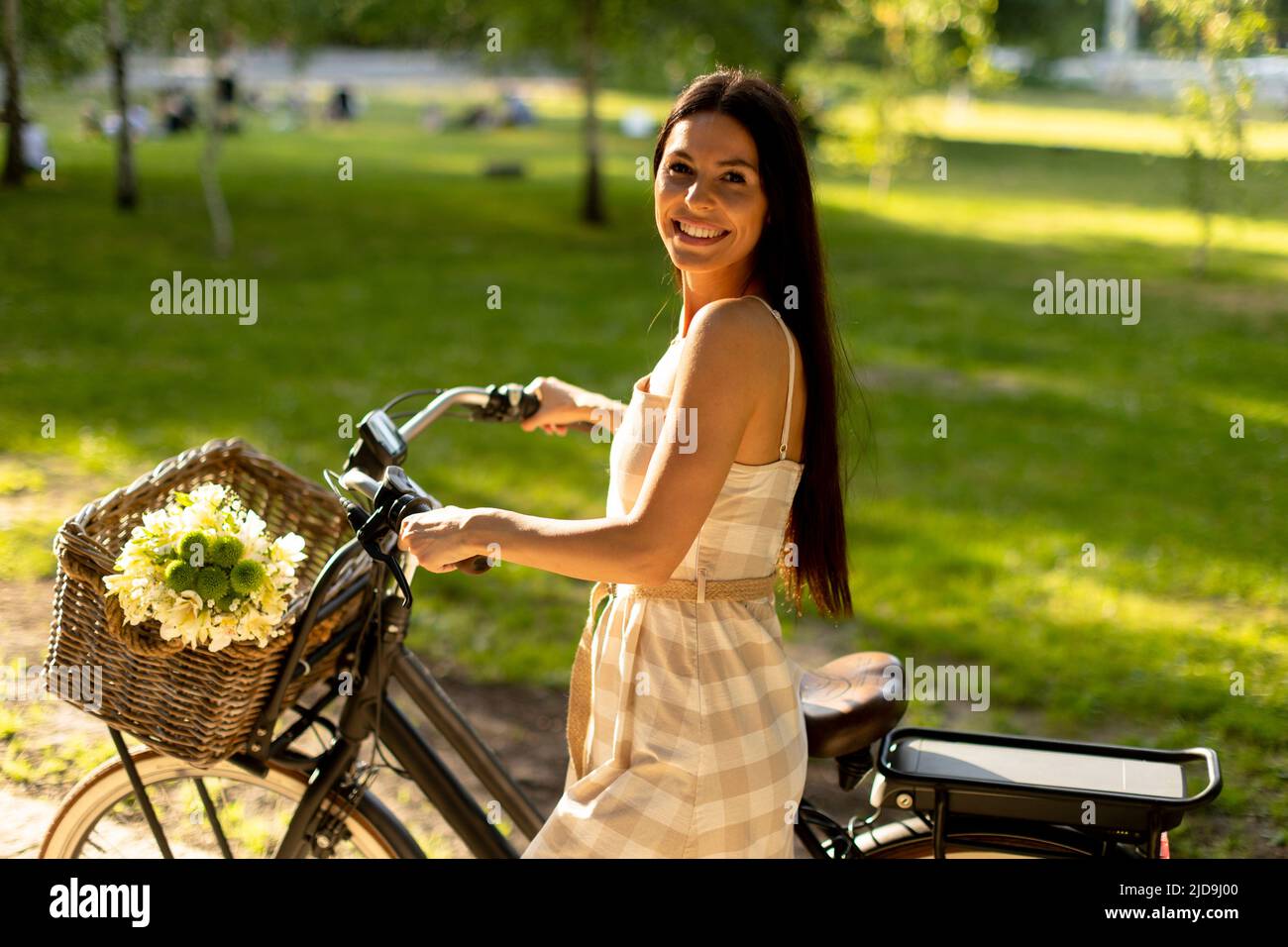 Jolie jeune femme avec des fleurs dans le panier de vélo électrique Banque D'Images