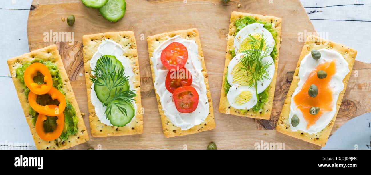 Vue de dessus de tout crackers avec différentes garnitures sur un panneau en bois. Banque D'Images